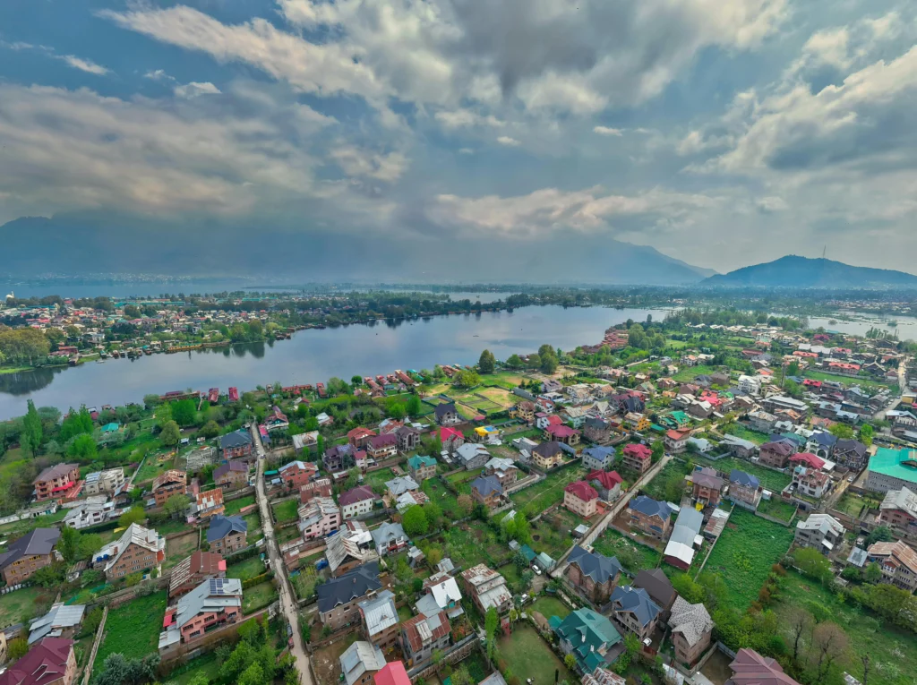 Aerial view of the city landscape and calm waters upon arrival at Srinagar, with mountains under a cloudy sky.