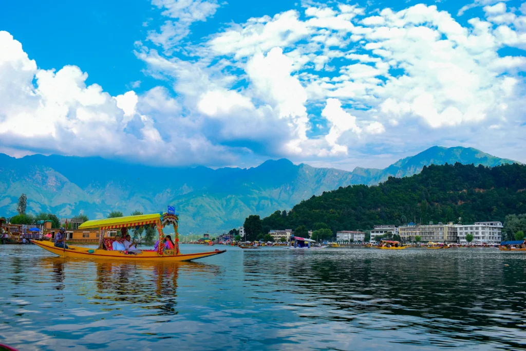 A yellow shikara boat carrying tourists on Dal Lake with mountains and blue sky in Srinagar.