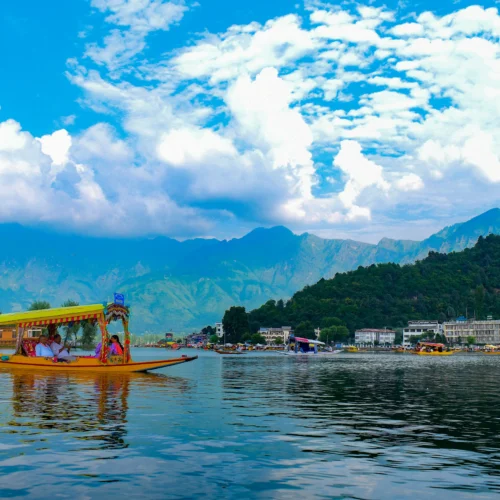 A yellow shikara boat carrying tourists on Dal Lake with mountains and blue sky in Srinagar.