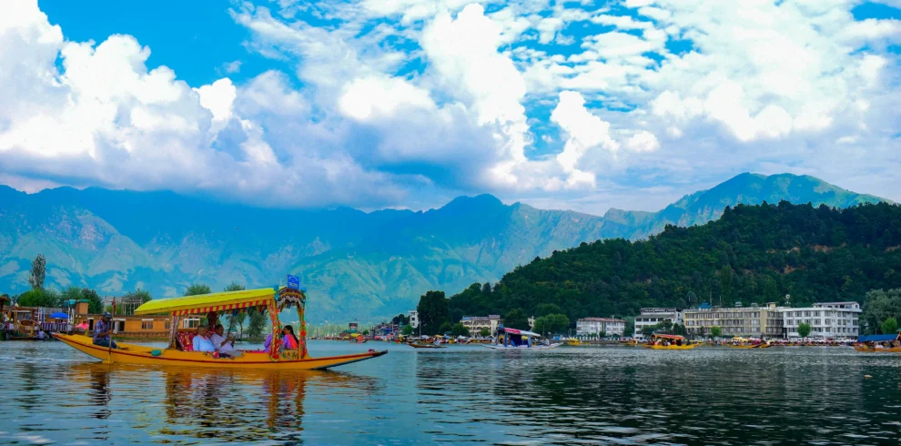 A yellow shikara boat carrying tourists on Dal Lake with mountains and blue sky in Srinagar.