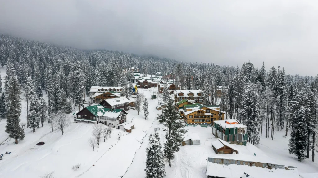 Snow-covered wooden houses and pine trees in a mountain village in Gulmarg, Kashmir.