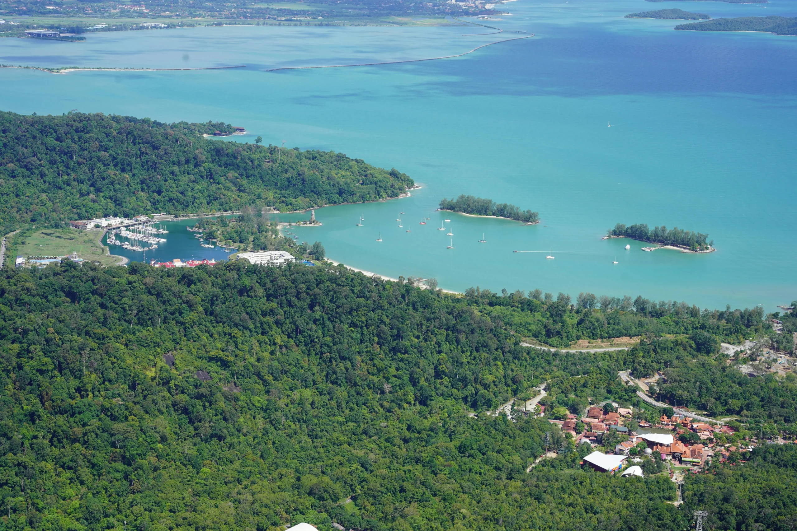 Aerial view of Langkawi, Malaysia, showing a coastal marina, turquoise Andaman Sea, and dense tropical green rainforest