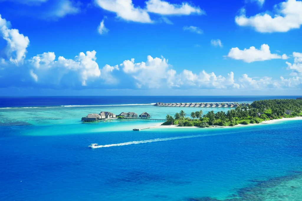 Luxurious overwater bungalows and a verdant tropical island encircled by the vivid blue waters of the Maldives are seen from above.