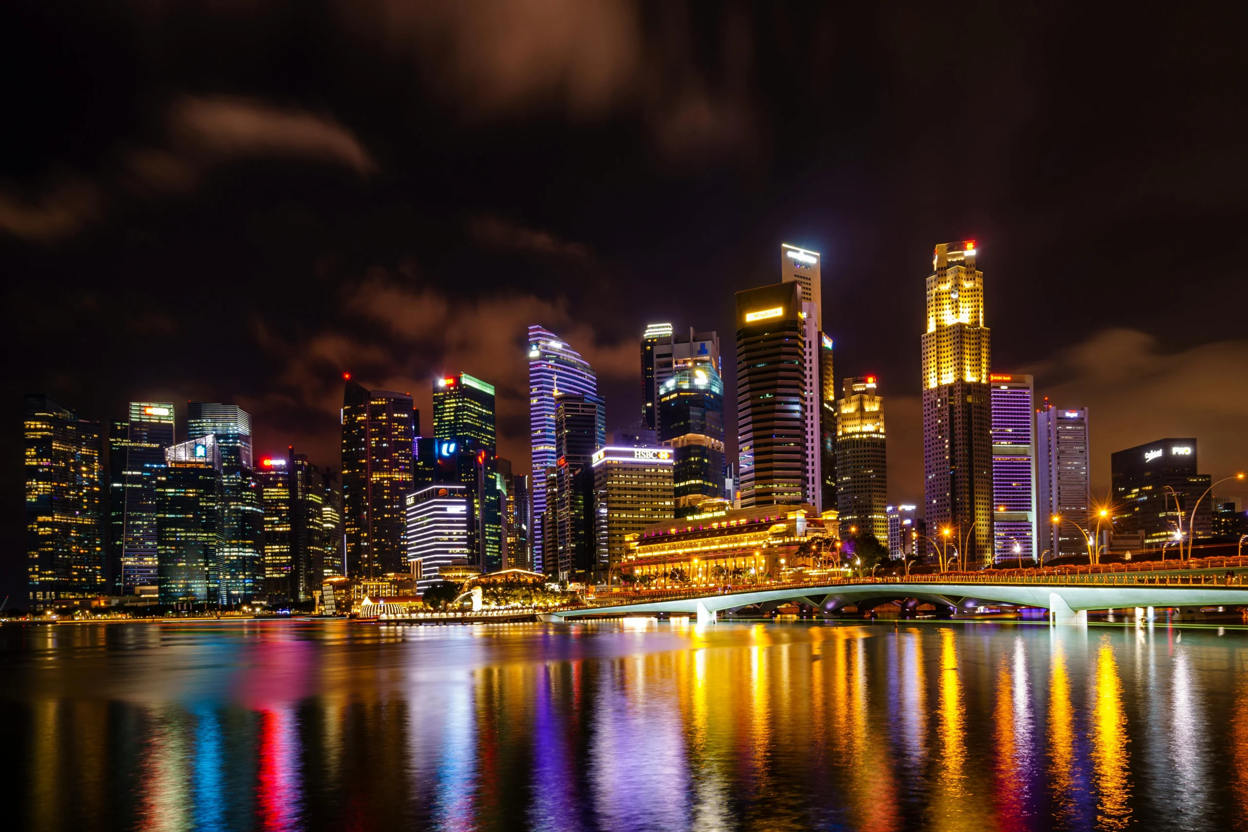 Singapore skyline at night with illuminated skyscrapers reflected in Marina Bay and the Esplanade Bridge.