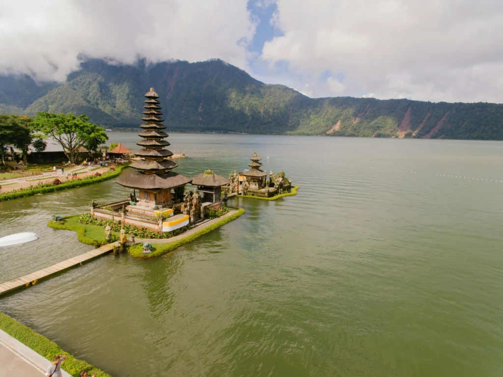 Pura Ulun Danu Beratan temple on Lake Beratan in Bali, with mountains and cloudy skies in the background.
