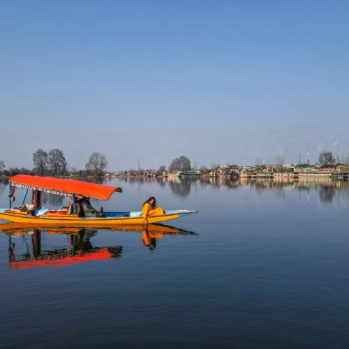 A colorful traditional Shikara boat with an orange canopy gliding on the calm, reflective waters of Dal Lake in Kashmir.