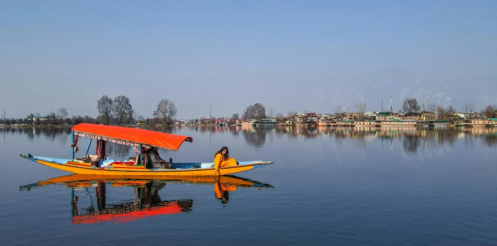 A colorful traditional Shikara boat with an orange canopy gliding on the calm, reflective waters of Dal Lake in Kashmir.